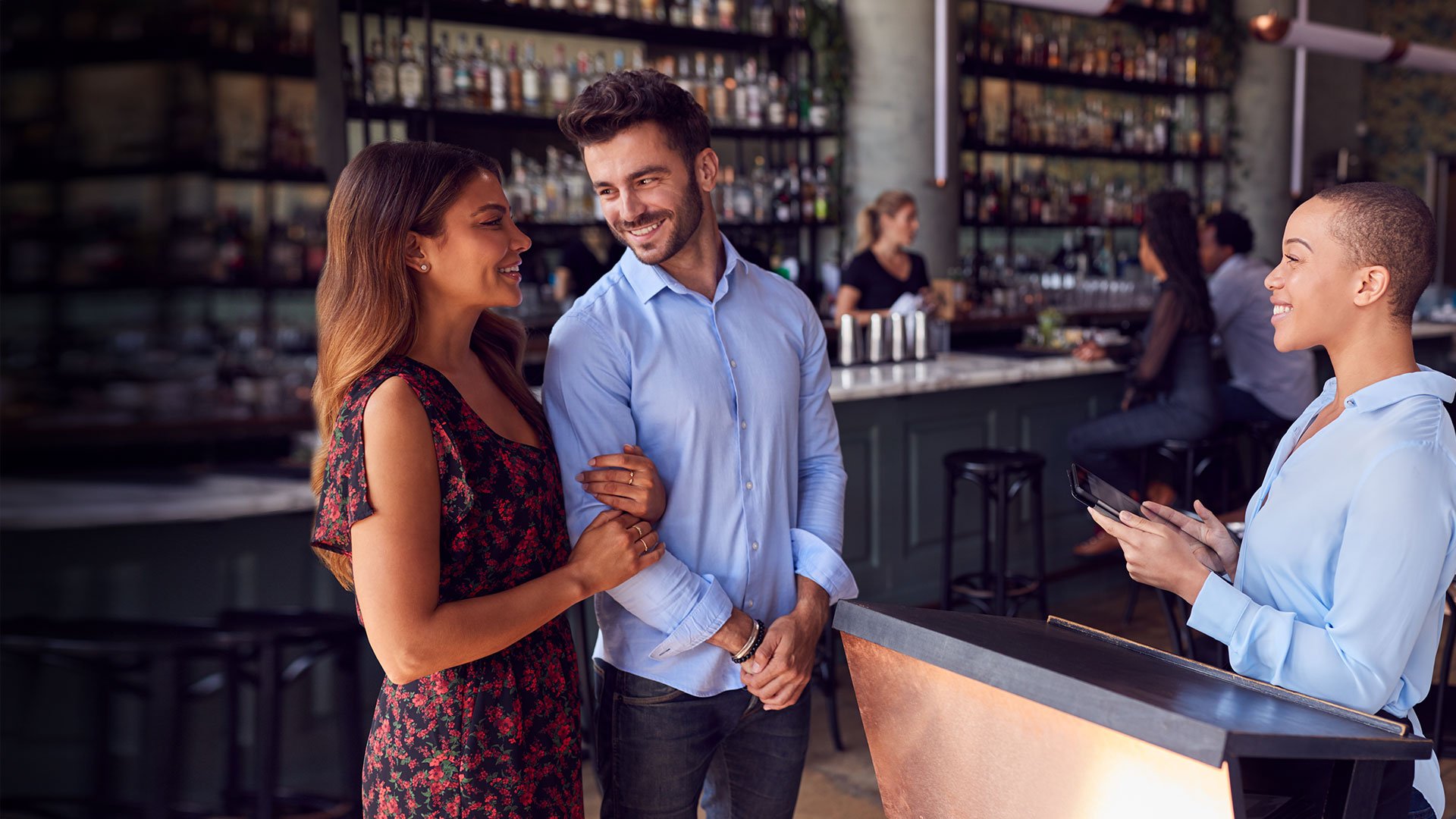 A waitress greeting a smiling couple at the front of a restaurant.
