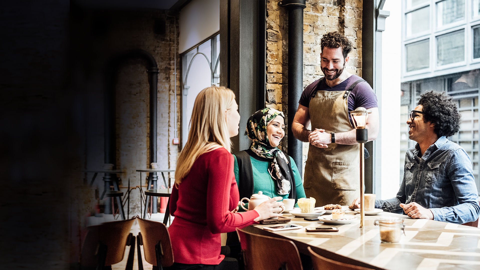Three people sitting at a restaurant table, with a waiter standing next to them.
